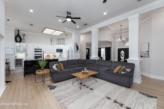 living room featuring ceiling fan with notable chandelier, light wood-type flooring, wine cooler, crown molding, and ornate columns