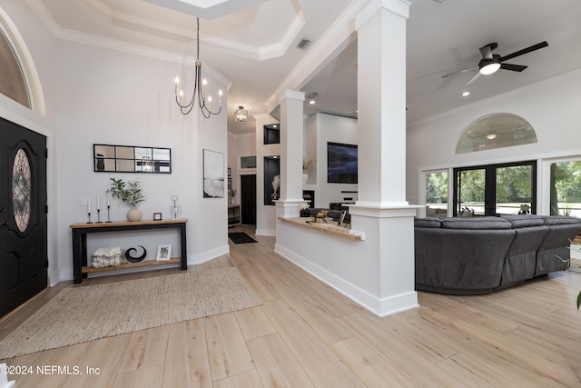 foyer featuring ornate columns, light hardwood / wood-style flooring, ceiling fan with notable chandelier, ornamental molding, and a raised ceiling