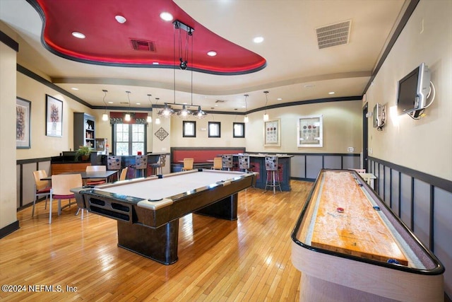 playroom featuring bar, ornamental molding, a tray ceiling, and light wood-type flooring