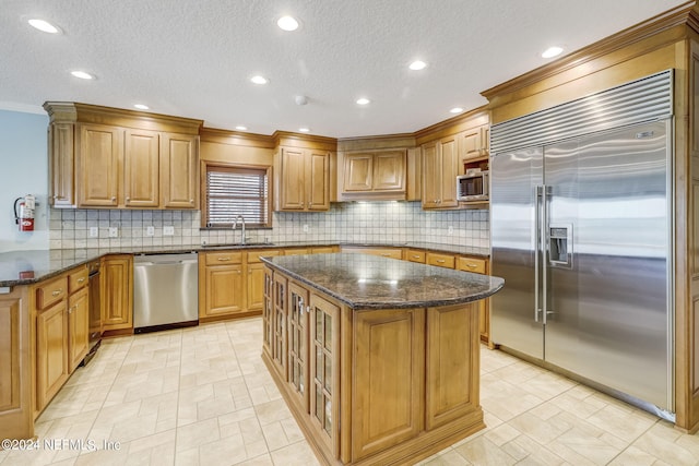 kitchen with dark stone counters, a center island, backsplash, and built in appliances