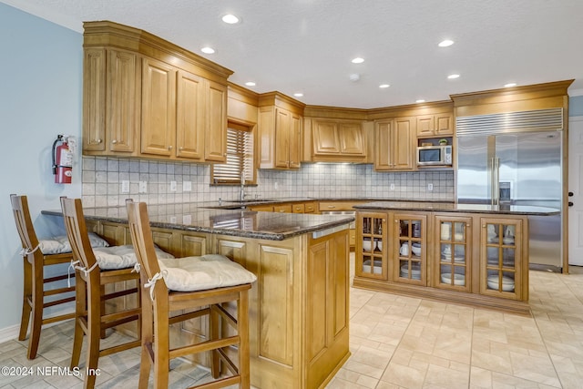 kitchen featuring a kitchen breakfast bar, dark stone countertops, light tile floors, tasteful backsplash, and built in appliances