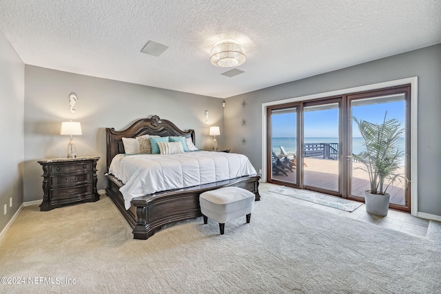 carpeted bedroom with a water view, access to exterior, and a textured ceiling