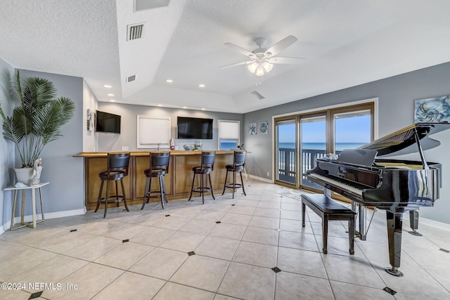 kitchen featuring a tray ceiling, ceiling fan, a breakfast bar, a water view, and a textured ceiling