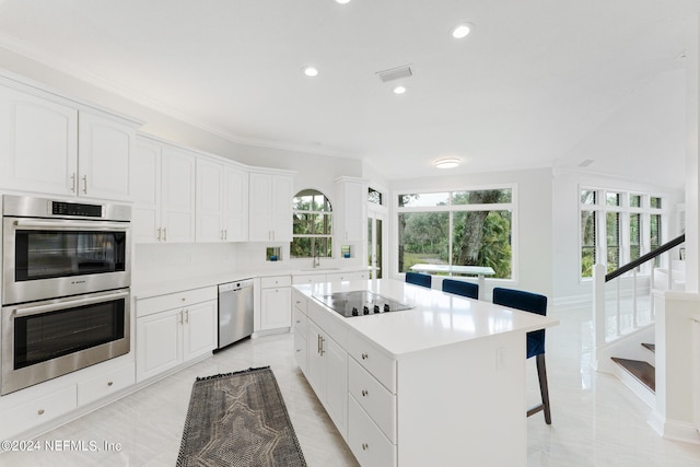 kitchen featuring a kitchen island, a breakfast bar area, light tile patterned floors, appliances with stainless steel finishes, and white cabinets