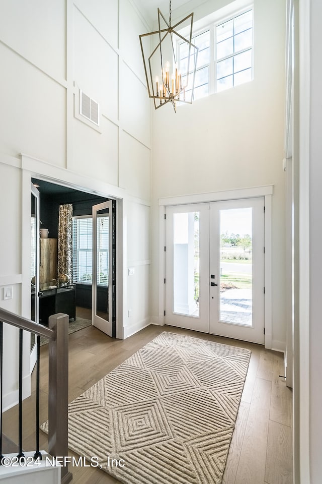 doorway with french doors, a notable chandelier, a towering ceiling, and hardwood / wood-style flooring