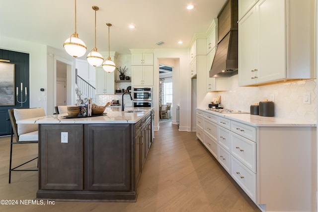 kitchen with a breakfast bar area, white cabinetry, hanging light fixtures, a center island with sink, and light stone countertops