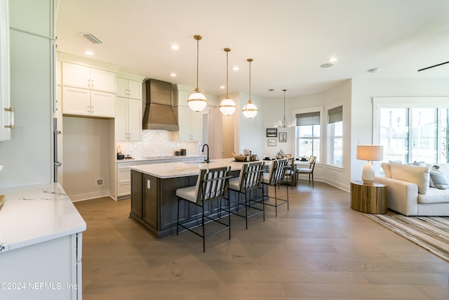 kitchen featuring premium range hood, a breakfast bar, decorative light fixtures, white cabinetry, and a kitchen island with sink