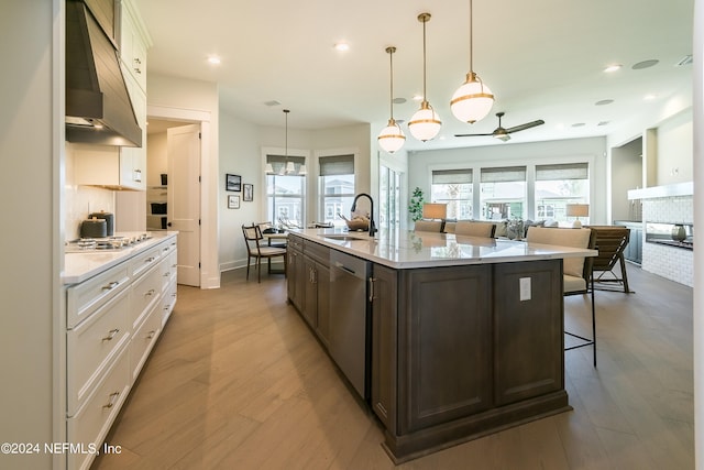 kitchen with a kitchen island with sink, sink, white cabinets, and decorative light fixtures