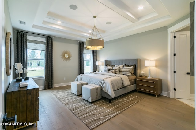 bedroom with multiple windows, light wood-type flooring, and a tray ceiling