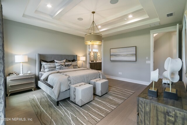 bedroom featuring hardwood / wood-style flooring, ensuite bathroom, and a raised ceiling