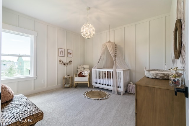 carpeted bedroom featuring a nursery area and a chandelier