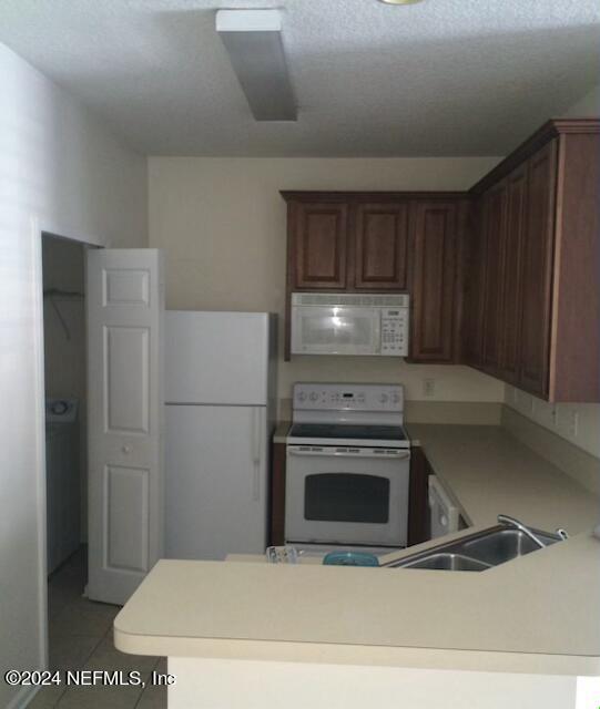 kitchen with kitchen peninsula, white appliances, sink, and light tile floors