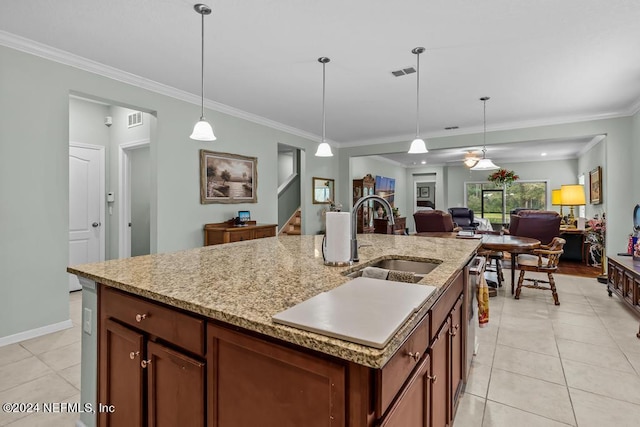 kitchen featuring pendant lighting, light tile flooring, ornamental molding, a kitchen island with sink, and sink