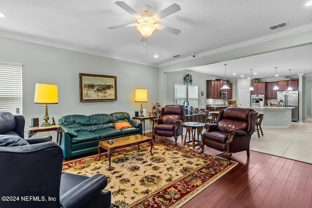 living room with light tile floors, plenty of natural light, ceiling fan, and ornamental molding