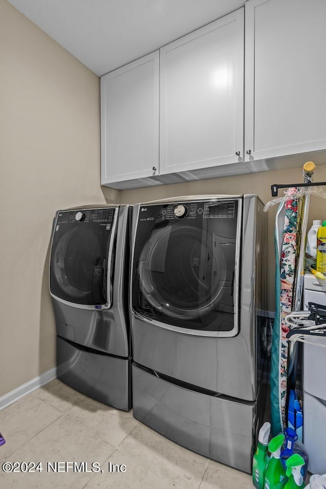 clothes washing area with light tile floors, cabinets, and washer and dryer