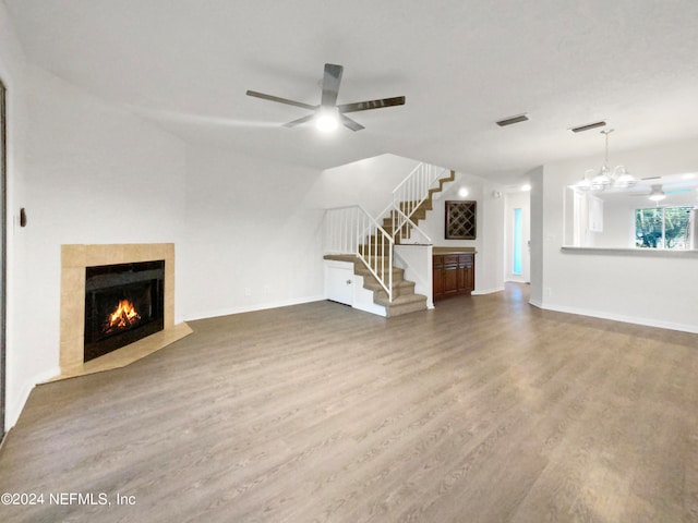 unfurnished living room with a tile fireplace, dark wood-type flooring, and ceiling fan with notable chandelier