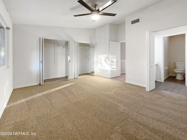 unfurnished bedroom featuring light colored carpet, connected bathroom, ceiling fan, and two closets