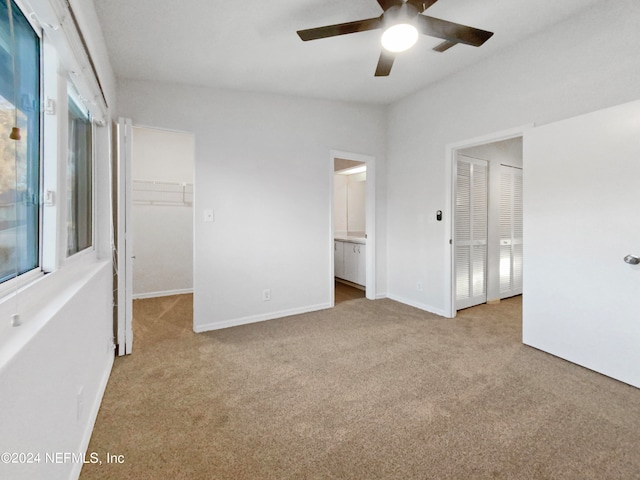 unfurnished bedroom featuring light carpet, a walk in closet, connected bathroom, and ceiling fan