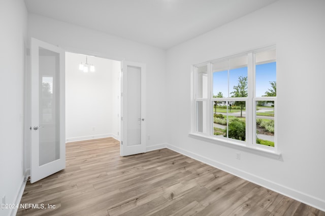 empty room with an inviting chandelier, light hardwood / wood-style flooring, and french doors