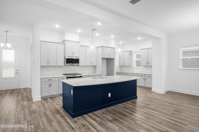 kitchen with appliances with stainless steel finishes, white cabinetry, sink, hanging light fixtures, and a center island with sink