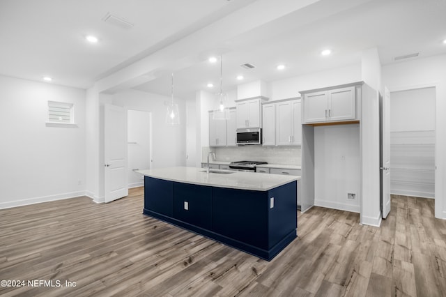 kitchen with appliances with stainless steel finishes, sink, white cabinets, hanging light fixtures, and a kitchen island with sink