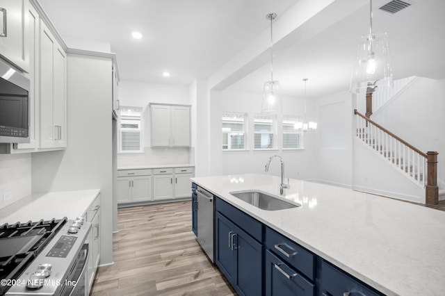 kitchen with sink, blue cabinetry, appliances with stainless steel finishes, white cabinets, and decorative light fixtures