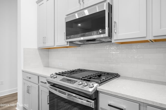 kitchen with backsplash, stainless steel appliances, light stone countertops, and white cabinets