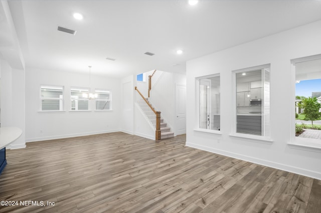 unfurnished living room with an inviting chandelier and hardwood / wood-style floors