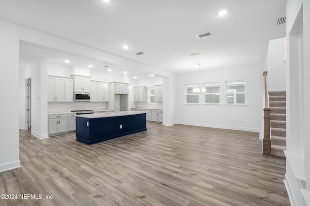 kitchen with an island with sink, appliances with stainless steel finishes, pendant lighting, and white cabinets