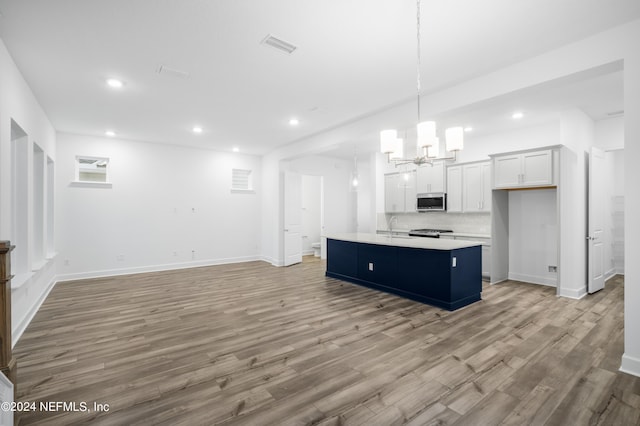 kitchen featuring appliances with stainless steel finishes, hanging light fixtures, an island with sink, white cabinets, and light wood-type flooring