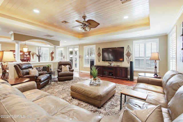 living area featuring wooden ceiling, wood finished floors, a tray ceiling, decorative columns, and crown molding