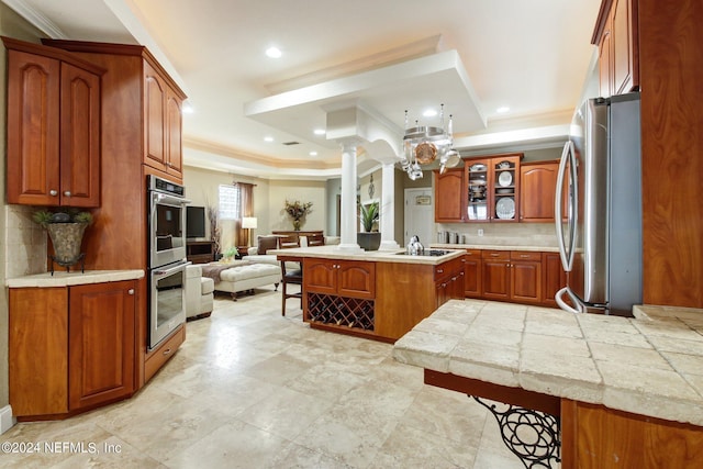 kitchen featuring a kitchen breakfast bar, open floor plan, appliances with stainless steel finishes, brown cabinets, and ornate columns