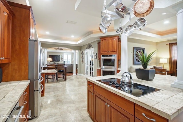 kitchen with stainless steel appliances, a tray ceiling, crown molding, and decorative columns