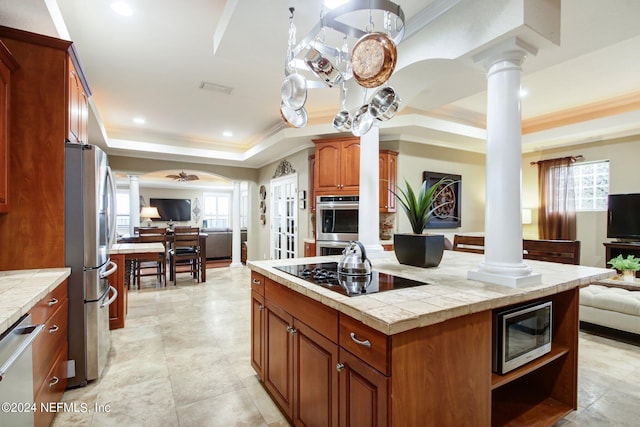 kitchen with ceiling fan, a tray ceiling, tile counters, stainless steel appliances, and decorative columns