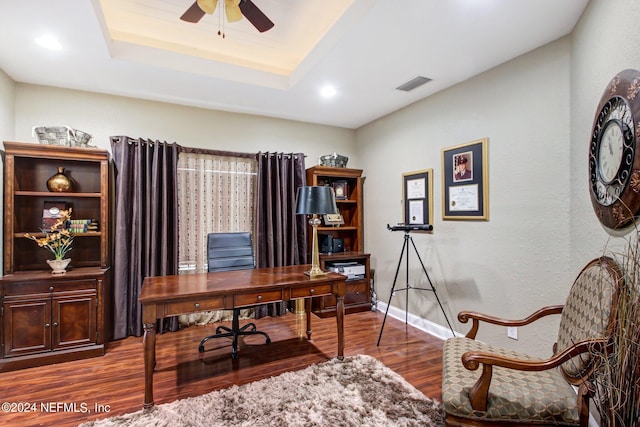 office area featuring baseboards, visible vents, a ceiling fan, wood finished floors, and a tray ceiling