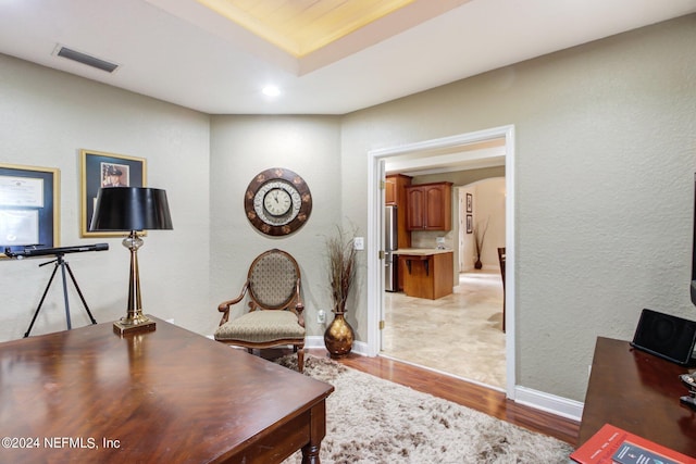 office area with a raised ceiling and light hardwood / wood-style flooring