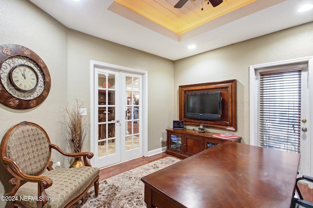 interior space featuring a textured wall, wood finished floors, a ceiling fan, french doors, and a tray ceiling