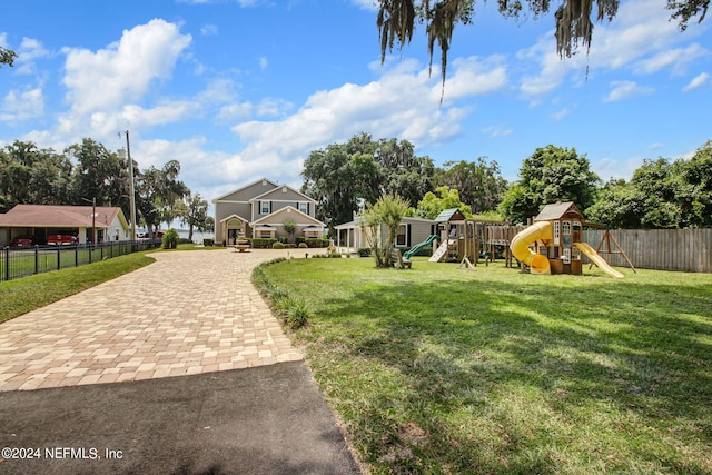 exterior space with decorative driveway, a playground, a lawn, and fence