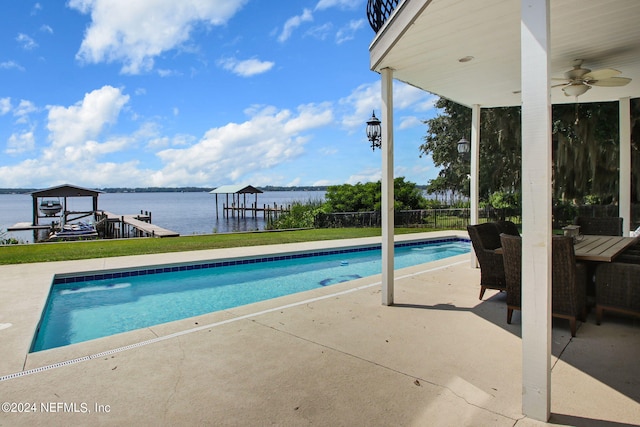 pool with a ceiling fan, a dock, a water view, and a patio