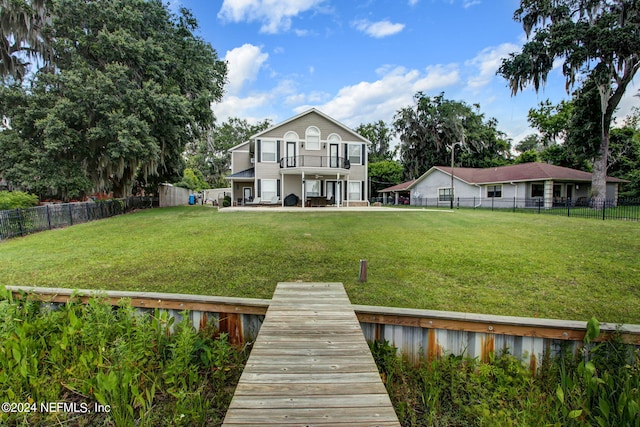 rear view of house featuring a balcony, a fenced backyard, and a lawn