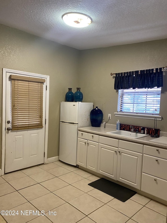 kitchen featuring light countertops, freestanding refrigerator, white cabinets, light tile patterned flooring, and a sink