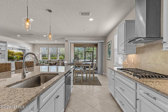 kitchen with wall chimney exhaust hood, hanging light fixtures, white cabinetry, and light stone counters