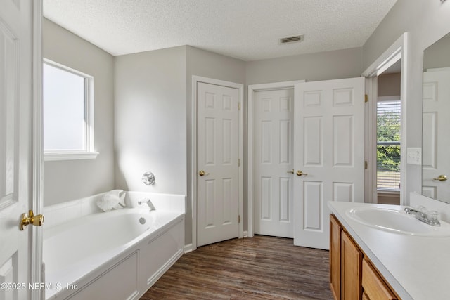 bathroom with hardwood / wood-style flooring, vanity, a textured ceiling, and a tub