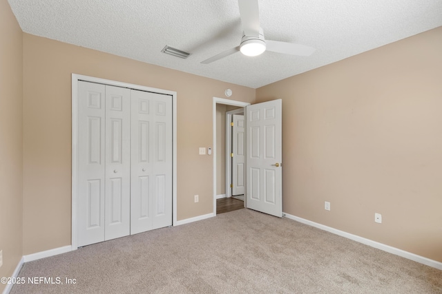 unfurnished bedroom featuring ceiling fan, light colored carpet, a textured ceiling, and a closet