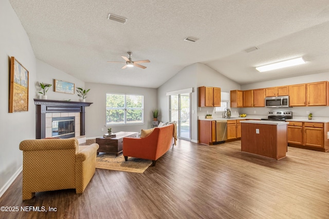 kitchen featuring sink, vaulted ceiling, light hardwood / wood-style floors, stainless steel appliances, and a tiled fireplace