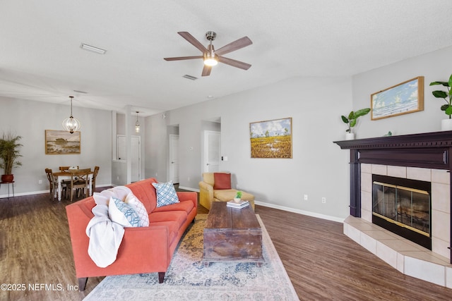 living room featuring ceiling fan, dark hardwood / wood-style flooring, a textured ceiling, and a tiled fireplace