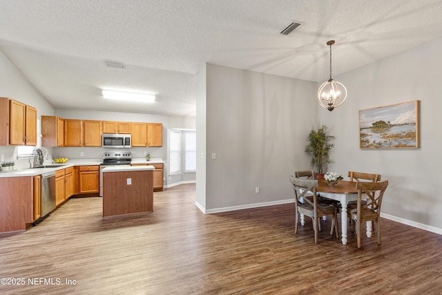 kitchen featuring appliances with stainless steel finishes, light hardwood / wood-style flooring, a notable chandelier, a kitchen island, and hanging light fixtures