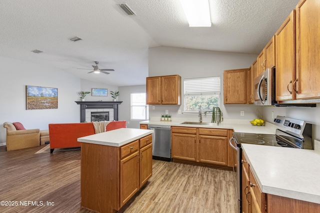 kitchen with sink, stainless steel appliances, a textured ceiling, a fireplace, and a kitchen island