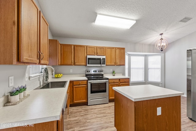 kitchen with an inviting chandelier, hanging light fixtures, sink, appliances with stainless steel finishes, and a kitchen island