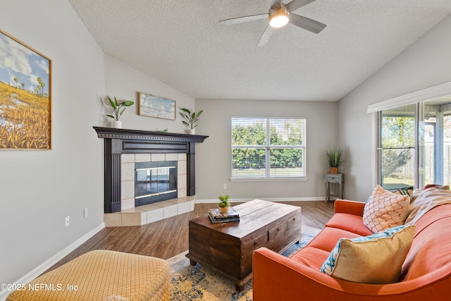 living room with wood-type flooring, a textured ceiling, ceiling fan, and a tiled fireplace